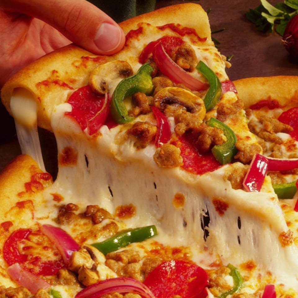 Hand pulling a slice of Mancino's pizza with melted cheese, sausage, mushrooms, and colorful peppers.