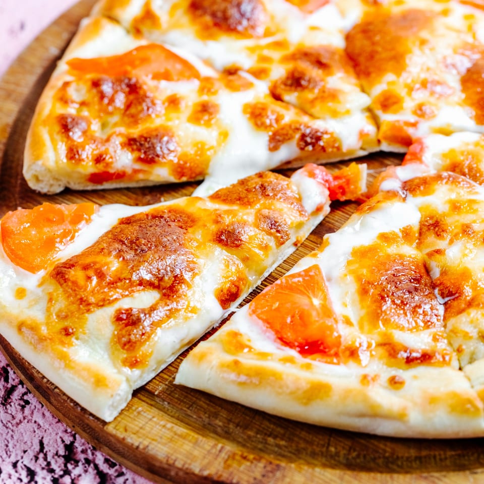 Close-up of a Mancino's pizza with melted cheese and tomato slices on a wooden board.