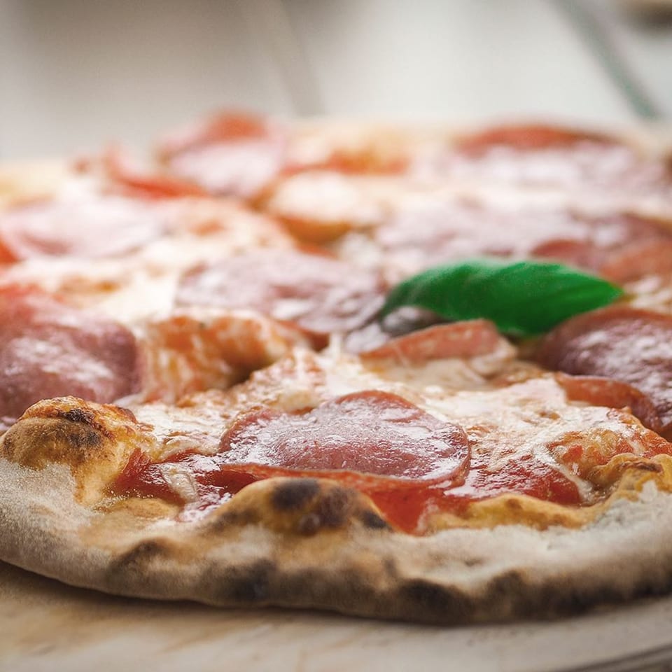 Close-up of a Mancino's pepperoni pizza with melted cheese, red sauce, and a basil leaf.