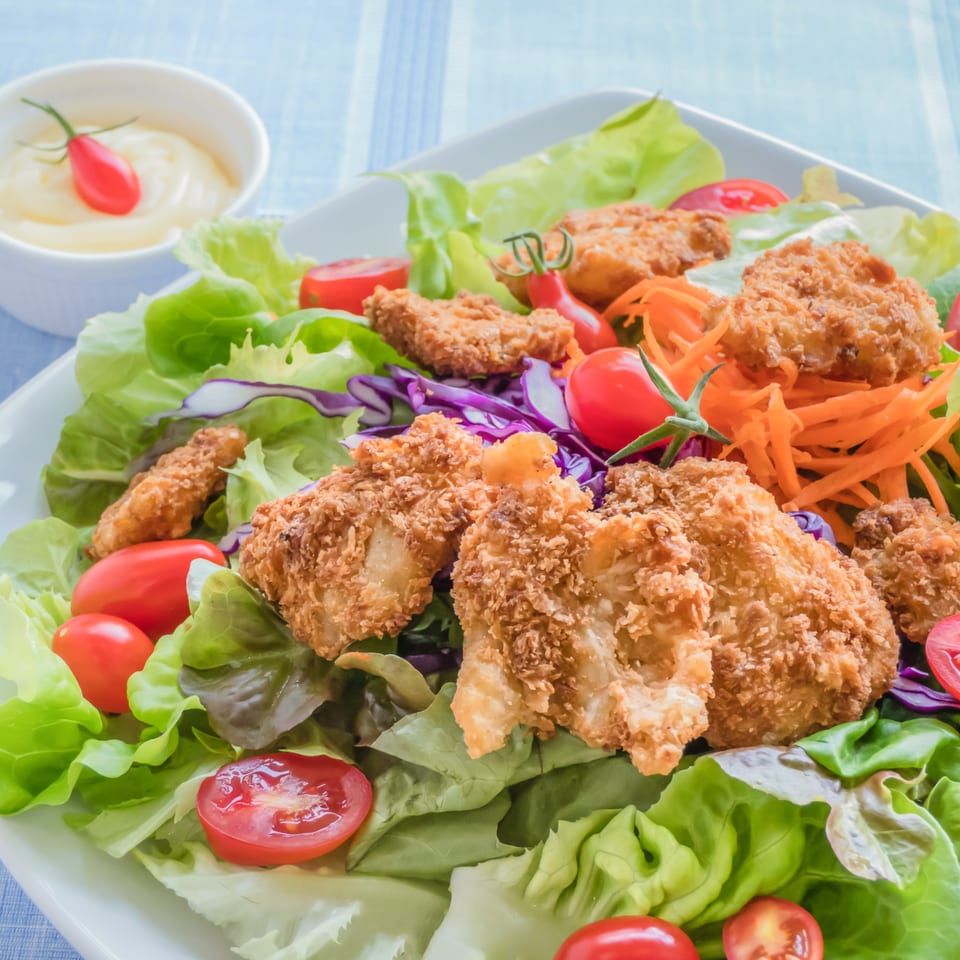 Crispy fried chicken salad with fresh greens, cherry tomatoes, shredded carrots, and purple cabbage.
